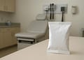 Paquete blanco en una mesa dentro de un consultorio médico, con una silla de examen y equipo médico visible en el fondo.