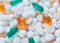 Una variedad de píldoras y cápsulas de diferentes colores y formas, incluyendo tabletas blancas, naranjas y verdes, dispuestas sobre una superficie clara.