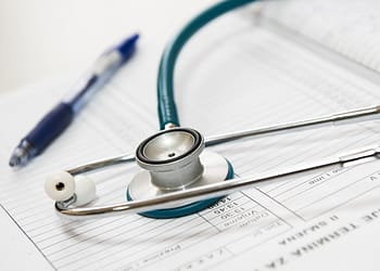 Steel and plastic stethoscope on sheets of paper with lines for notes. On top is a pen.
