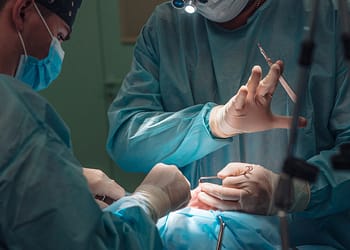 Two surgeons in a surgical setting, wearing masks and gloves, are performing an operation, using surgical instruments.