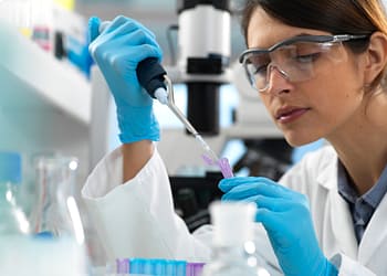 Laboratory woman with blue gloves using a micropipette to fill a test tube in a laboratory setting.