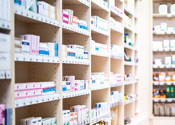 Shelves in a pharmacy with various products in boxes, including medications and personal care products.