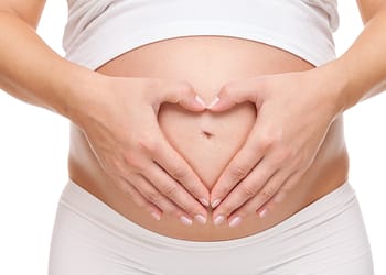 A pregnant woman forms a heart with her hands on her abdomen.