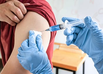 Person receiving an injection in the arm, with one hand holding the syringe and the other holding the upper arm.