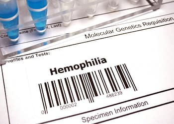 Label on a genetic application form showing the word "Hemophilia" and a barcode, with test tubes in the background.