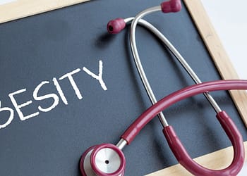 A red stethoscope on a black board with the word "OBESITY" written in white letters.