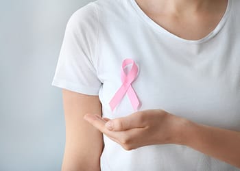 Person wearing a white t-shirt displaying a pink ribbon on the left side of the chest, with the right hand extended forward.
