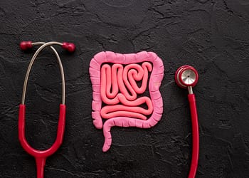 A pink clay model of an intestine placed on a dark surface, next to a red stethoscope also resting on the same surface.