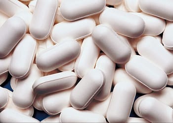 A large number of elongated white tablets stacked on top of each other.