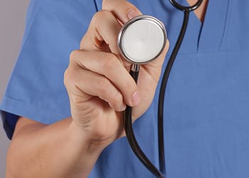 Stethoscope in the hand of a health professional in a blue uniform.