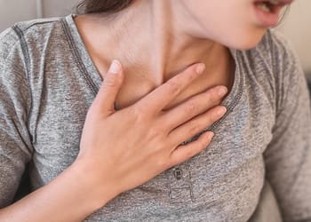 Woman with hand on chest, showing signs of difficulty breathing.