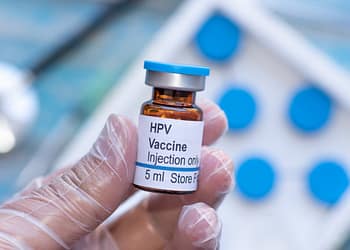 HPV vaccine vial in a gloved hand, labeled "Injection Only" and with a volume of 5 mL.