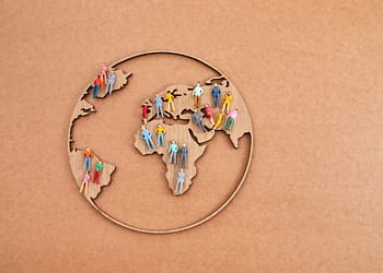 Wooden world map with colored human figures representing different people, on a brown background.