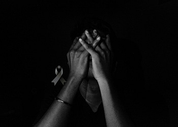 A person with their hands on their face, in a dark environment, with a black bow superimposed on the image.