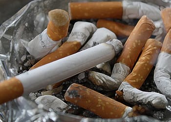 Cenicero con colillas de cigarrillos, algunos de ellos quemados, y un cigarrillo sin encender en primer plano.