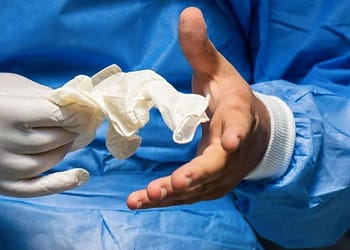 Mano con guante de látex sosteniendo un guante desechado, en un entorno sanitario.