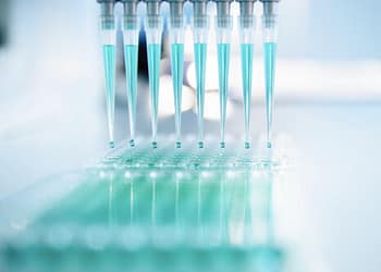 Automatic pipettes filling a laboratory dish with blue liquid.