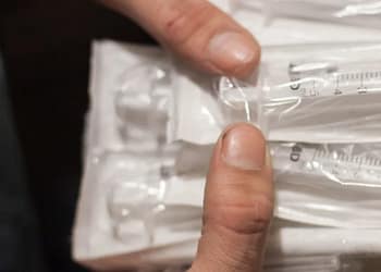 A hand holds a package of syringes in plastic wrap, several in a row, showing their measurement markings.