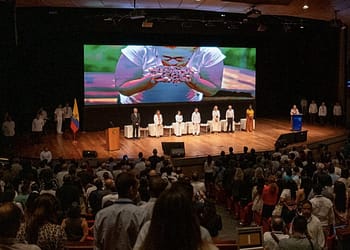 Panoramic view of the Second World Conference on Air Pollution and Health, with a lectern in the foreground and a large audience in the auditorium, where several flags and a screen presentation can be seen behind the speakers on stage.