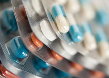 Paquetes de medicamentos con cápsulas de diferentes colores, incluidos azul, blanco y naranja, dispuestos en filas.
