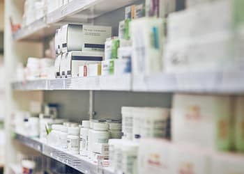 Shelves in a pharmacy with various medicine containers, some embellished and others in white bottles. The image is slightly out of focus.