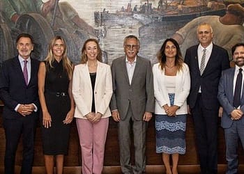 Group of eight people posing in front of a mural, with a mix of formal attire and diverse features.