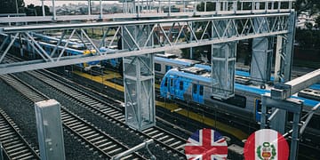 An aerial view of a train station with tracks and parked blue trains, surrounded by an urban environment and metal support structures.