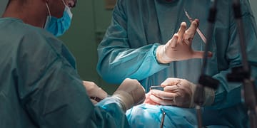 Two surgeons in a surgical setting, wearing masks and gloves, are performing an operation, using surgical instruments.