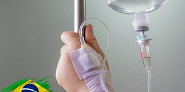 Patient's hand with a drip connected to a stand, in a clinical setting. Blurred background.
