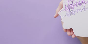 A hand holds a paper cut in the shape of a human profile, with purple lines simulating waves at the top, on a lilac background.