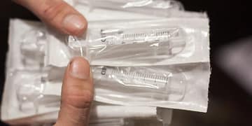 A hand holds a package of syringes in plastic wrap, several in a row, showing their measurement markings.