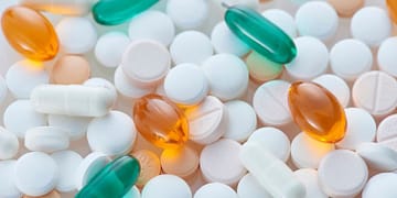 A variety of pills and capsules of different colors and shapes, including white, orange, and green tablets, arranged on a clear surface.