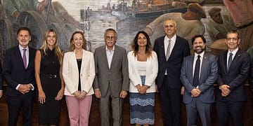 Group of eight people posing in front of a mural, with a mix of formal attire and diverse features.