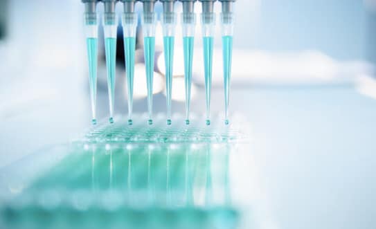 Automatic pipettes filling a laboratory dish with blue liquid.