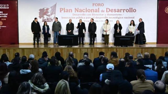 A group of people standing on a stage during a forum titled "National Development Plan", with an audience sitting in front of them.