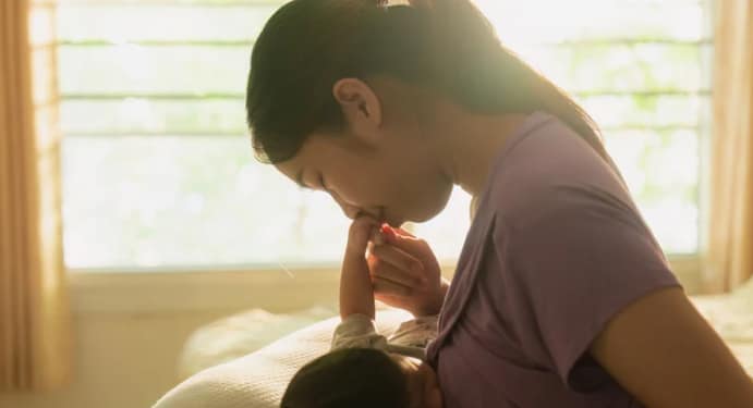 Woman holding and breastfeeding a baby in a naturally lit environment.