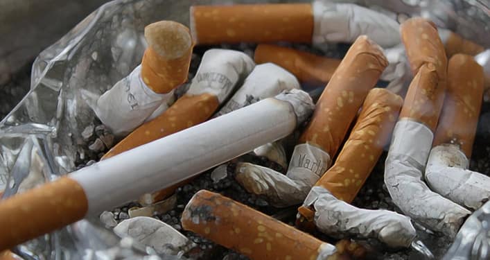Cenicero con colillas de cigarrillos, algunos de ellos quemados, y un cigarrillo sin encender en primer plano.