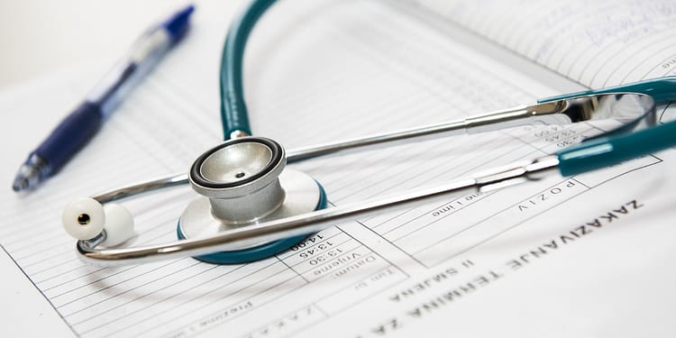 Steel and plastic stethoscope on sheets of paper with lines for notes. On top is a pen.