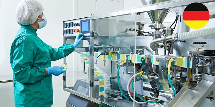 Operator in protective clothing checking a machine in an industrial environment, equipped with control panels and pipes.