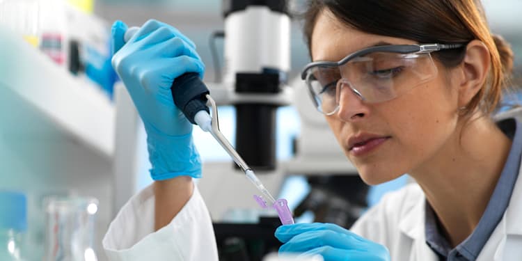 Laboratory woman with blue gloves using a micropipette to fill a test tube in a laboratory setting.