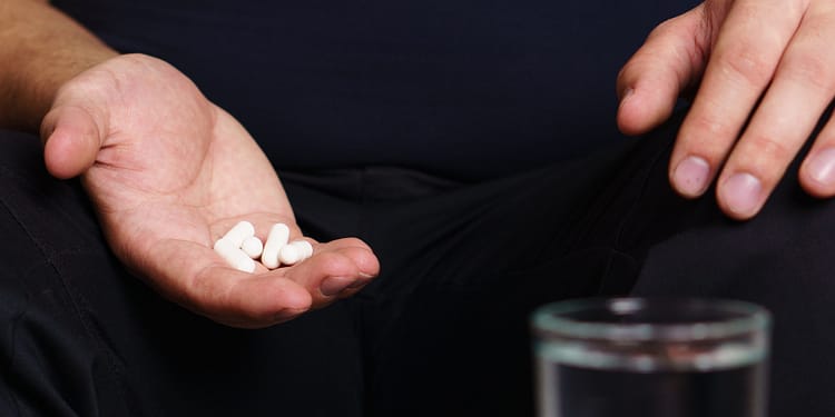 Man sitting holding white pills in one hand, with a glass of water nearby.