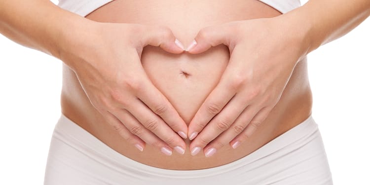 A pregnant woman forms a heart with her hands on her abdomen.