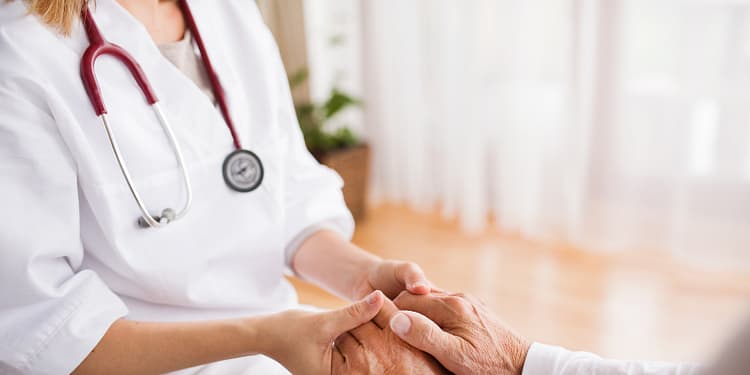 A person in a doctor's coat holds a patient's hand in a bright and welcoming environment.