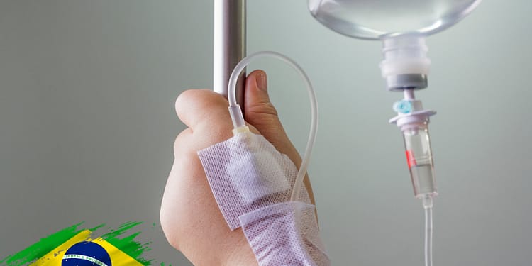 Patient's hand with a drip connected to a stand, in a clinical setting. Blurred background.