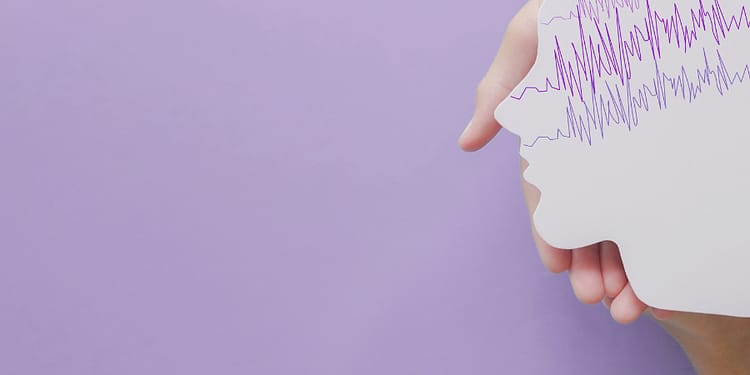 A hand holds a paper cut in the shape of a human profile, with purple lines simulating waves at the top, on a lilac background.