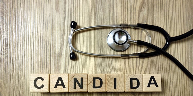 Bloques de madera con la palabra 'CANDIDA' dispuestos sobre una superficie de madera, con un estetoscopio colocado parcialmente encima de ellos.