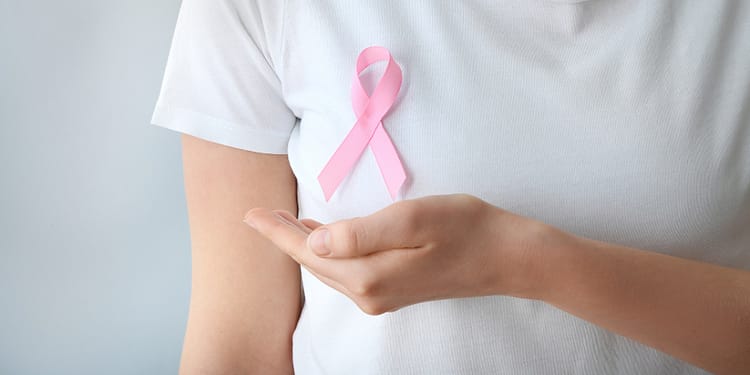 Person wearing a white t-shirt displaying a pink ribbon on the left side of the chest, with the right hand extended forward.