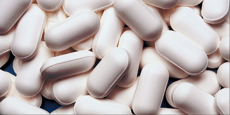 A large number of elongated white tablets stacked on top of each other.