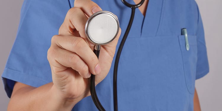 Stethoscope in the hand of a health professional in a blue uniform.