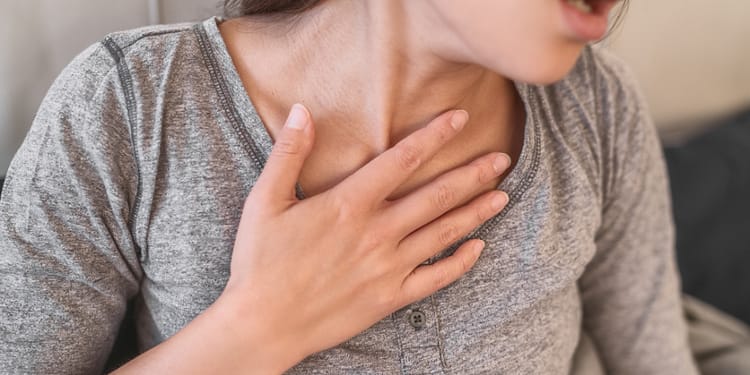 Mujer con la mano en el pecho, mostrando signos de dificultad para respirar.